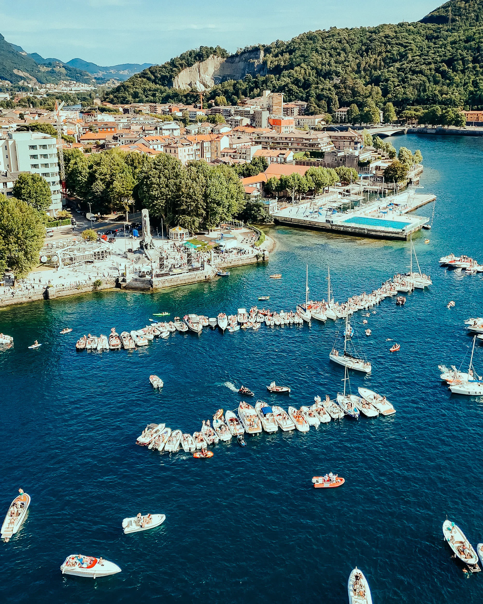 Vista dall'alto delle barche di The Waves 2025 in fila sul lago blu, con il paese sullo sfondo